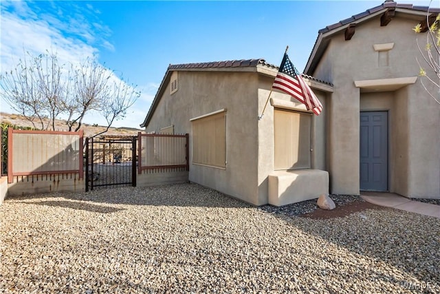 view of property exterior featuring a tile roof, fence, a gate, and stucco siding