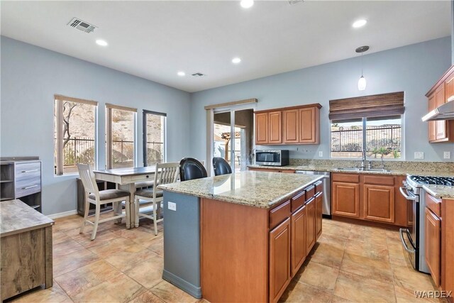 kitchen featuring a center island, decorative light fixtures, stainless steel appliances, visible vents, and brown cabinetry