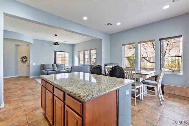 kitchen featuring visible vents, a kitchen island, light stone counters, brown cabinets, and open floor plan