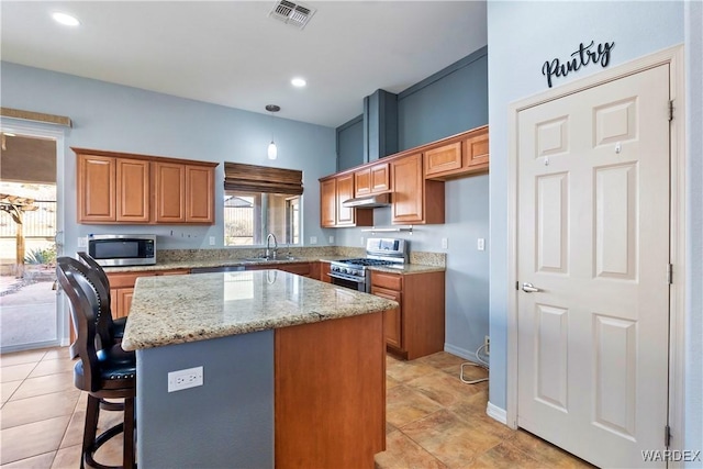 kitchen with light stone counters, brown cabinets, visible vents, appliances with stainless steel finishes, and a kitchen island