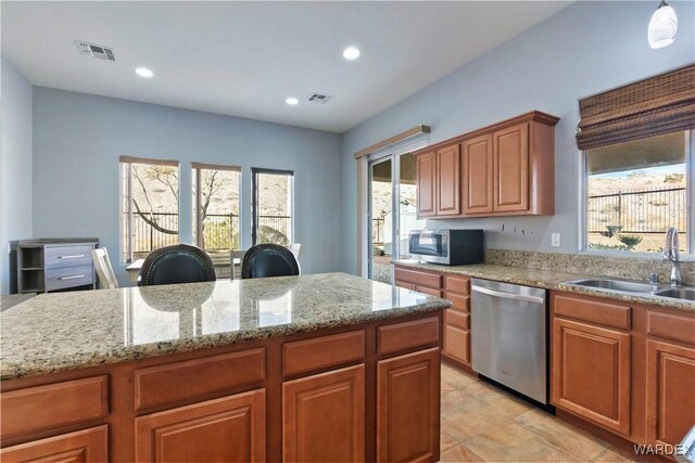 kitchen with visible vents, brown cabinetry, light stone counters, appliances with stainless steel finishes, and a sink