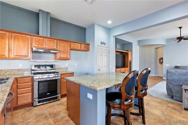 kitchen featuring a center island, appliances with stainless steel finishes, open floor plan, light stone countertops, and under cabinet range hood