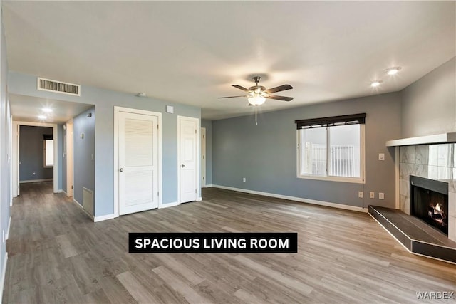 unfurnished living room with wood finished floors, a tile fireplace, visible vents, and baseboards