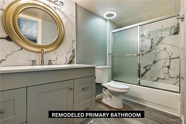 full bath with combined bath / shower with glass door, vanity, toilet, and wood finished floors