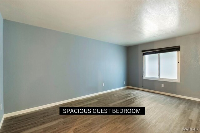 empty room featuring a textured ceiling, wood finished floors, and baseboards