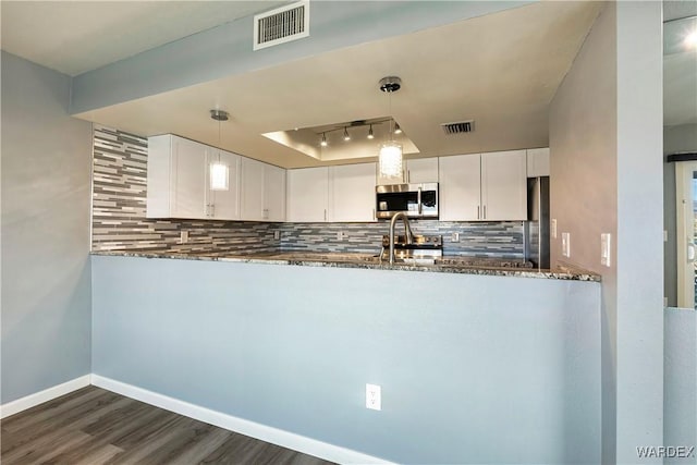 kitchen featuring tasteful backsplash, visible vents, dark stone counters, stainless steel microwave, and a tray ceiling