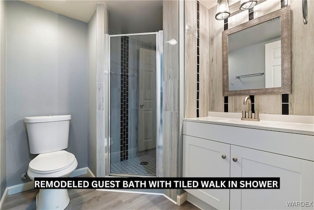 bathroom with toilet, a stall shower, vanity, wood finished floors, and baseboards