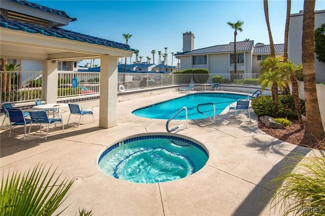 pool with a patio area, fence, and a hot tub