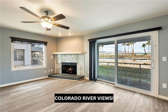 unfurnished living room featuring a tiled fireplace, wood finished floors, a wealth of natural light, and baseboards