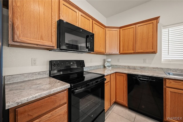 kitchen with light tile patterned floors, black appliances, light stone counters, and brown cabinetry