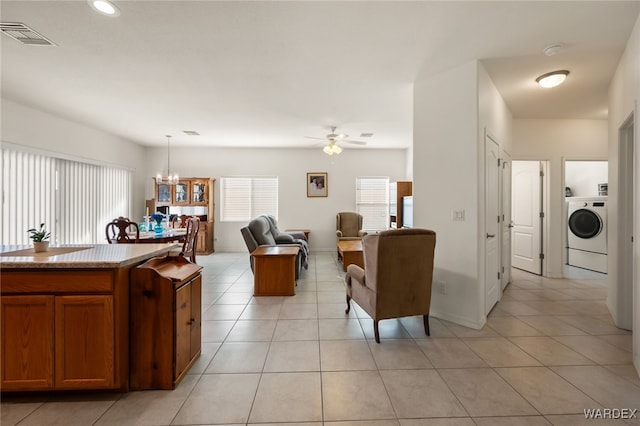 living area with light tile patterned floors, visible vents, baseboards, washer / clothes dryer, and ceiling fan with notable chandelier