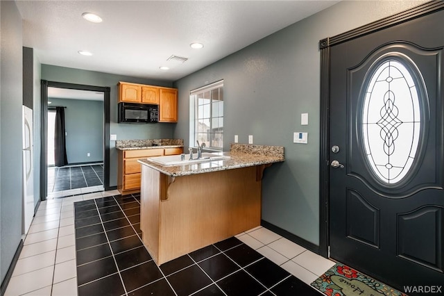 kitchen featuring black microwave, a peninsula, dark tile patterned floors, visible vents, and a kitchen breakfast bar