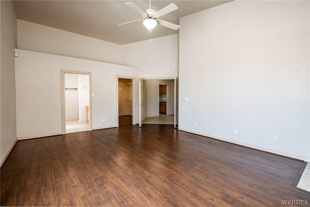 unfurnished bedroom featuring a high ceiling, dark wood-style flooring, a walk in closet, and baseboards