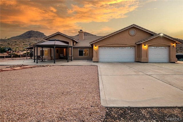 view of front of property featuring a chimney, a tiled roof, an attached garage, a mountain view, and stucco siding