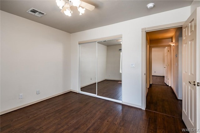 unfurnished bedroom with dark wood finished floors, a closet, visible vents, a ceiling fan, and baseboards