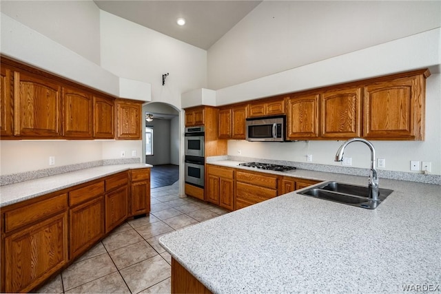 kitchen with arched walkways, brown cabinetry, appliances with stainless steel finishes, light countertops, and a sink