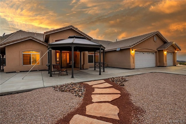 exterior space with a garage, a tile roof, a gazebo, and stucco siding