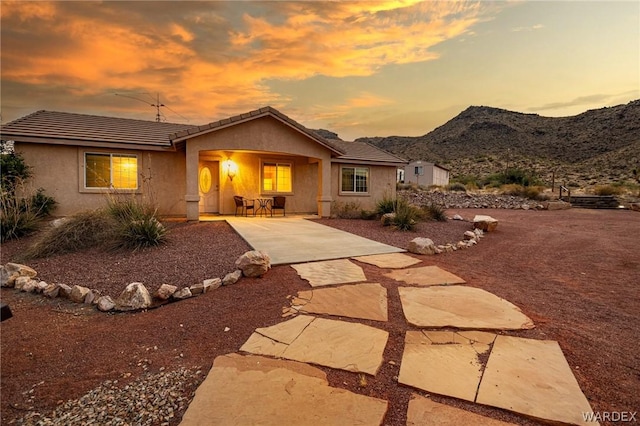 back of property at dusk featuring a tile roof, stucco siding, a mountain view, and a patio