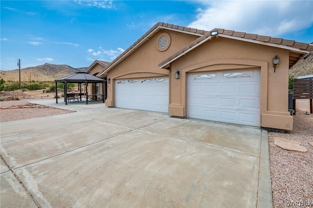 view of front of property with concrete driveway, an attached garage, a gazebo, a mountain view, and stucco siding