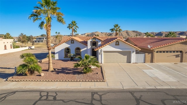 mediterranean / spanish house with a garage, concrete driveway, a tile roof, a mountain view, and stucco siding