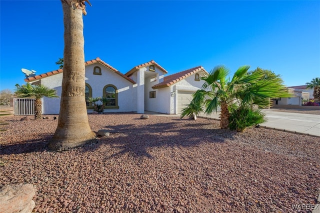 mediterranean / spanish house featuring a tile roof, an attached garage, and stucco siding