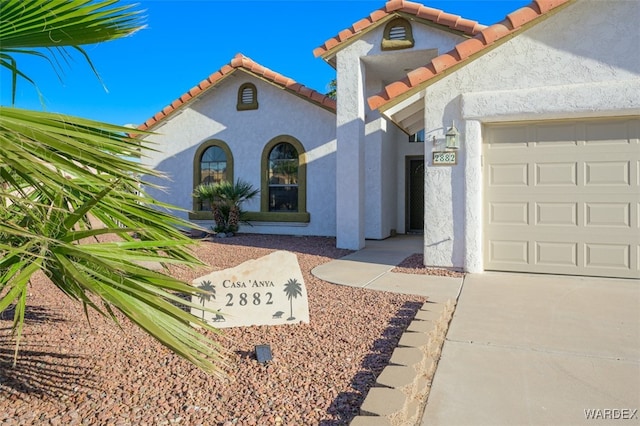 mediterranean / spanish-style home with a garage, a tiled roof, and stucco siding