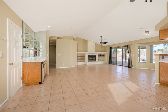 unfurnished living room featuring light tile patterned floors, a ceiling fan, a glass covered fireplace, lofted ceiling, and a sink