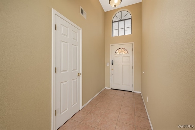 foyer with light tile patterned floors, a high ceiling, visible vents, and baseboards