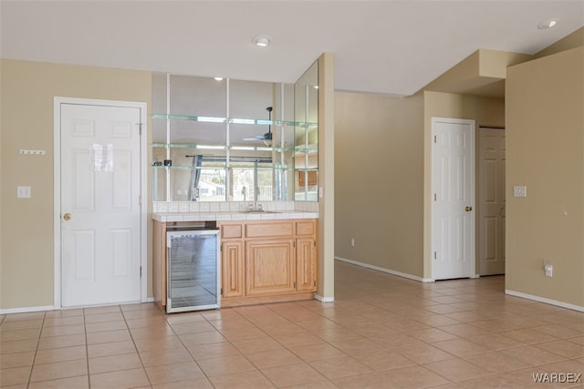 bar with light tile patterned floors, wine cooler, a sink, and baseboards