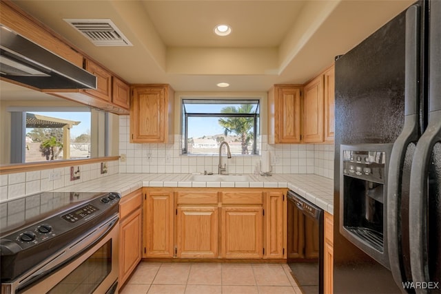 kitchen featuring tile counters, visible vents, a tray ceiling, black appliances, and a sink