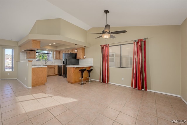 kitchen with light countertops, black fridge with ice dispenser, decorative backsplash, a sink, and a peninsula