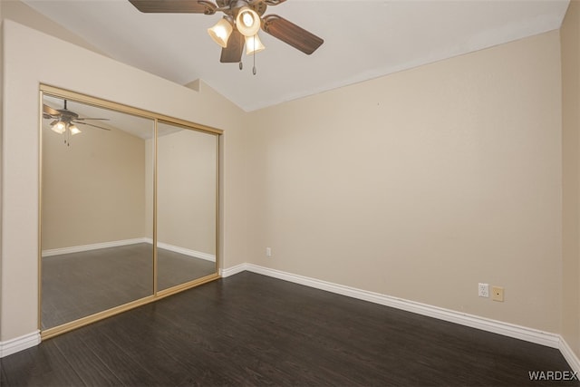 unfurnished bedroom featuring dark wood-style flooring, a closet, a ceiling fan, vaulted ceiling, and baseboards