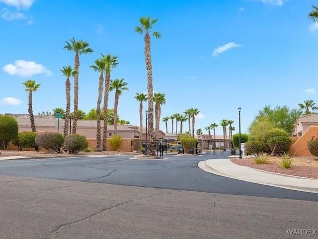 view of street with a gate, sidewalks, curbs, street lights, and a gated entry