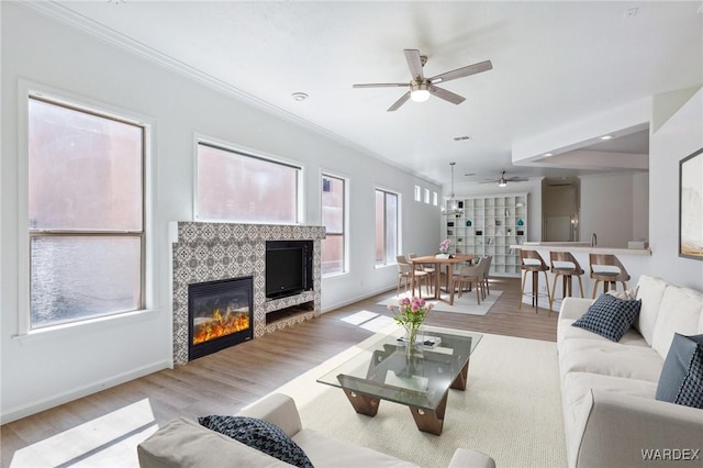 living room with wood finished floors, baseboards, ceiling fan, ornamental molding, and a tiled fireplace