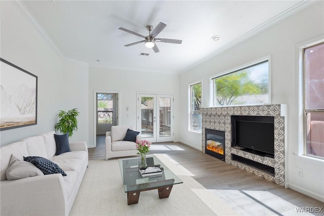 living room with a ceiling fan, baseboards, wood finished floors, a tile fireplace, and ornamental molding