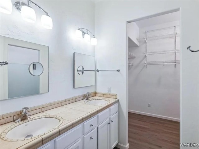 bathroom featuring a walk in closet, double vanity, baseboards, and a sink