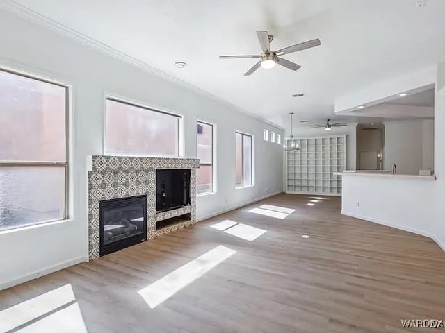 unfurnished living room with a healthy amount of sunlight, a tile fireplace, a ceiling fan, and wood finished floors