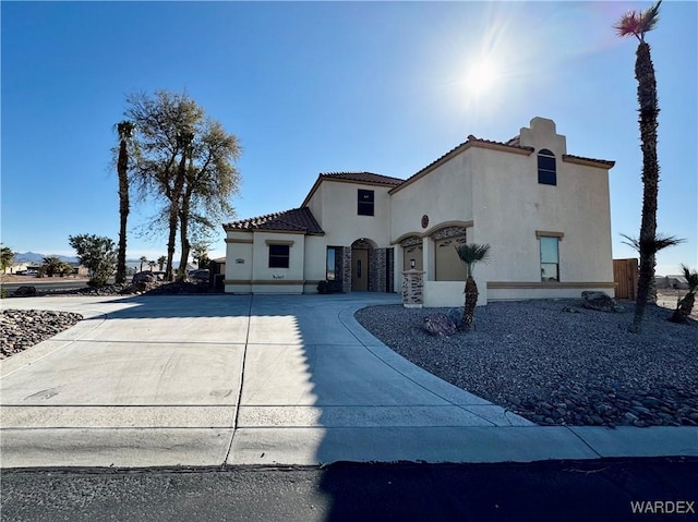 mediterranean / spanish home with concrete driveway, stone siding, a tile roof, and stucco siding