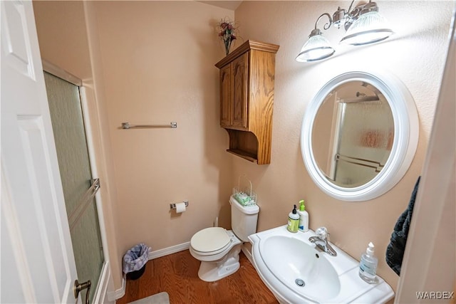 full bathroom featuring toilet, a shower with door, a sink, and wood finished floors