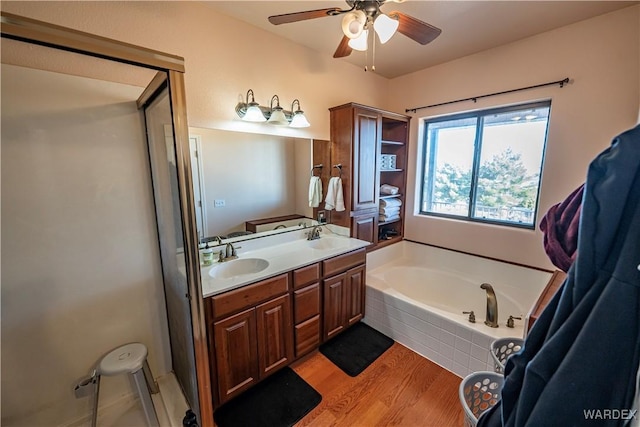 bathroom with double vanity, a garden tub, a sink, and wood finished floors