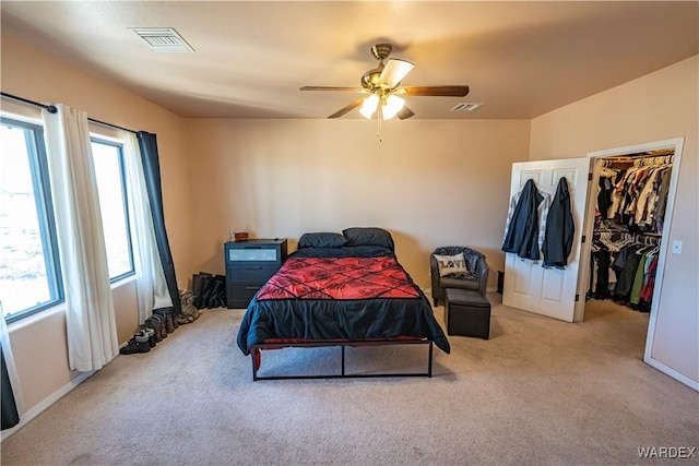 carpeted bedroom featuring visible vents, a walk in closet, and a ceiling fan