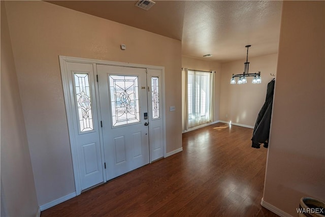 entryway featuring a notable chandelier, dark wood finished floors, visible vents, a textured ceiling, and baseboards