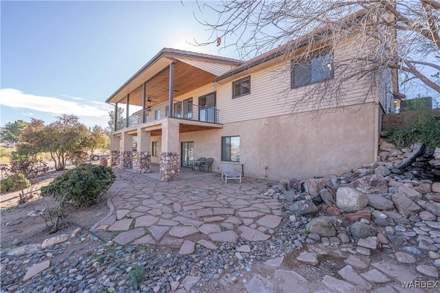 back of house with a patio area, stucco siding, a balcony, and a ceiling fan