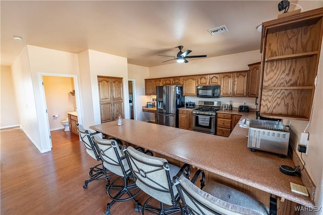 kitchen featuring visible vents, brown cabinetry, appliances with stainless steel finishes, a kitchen breakfast bar, and a peninsula