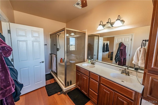 full bathroom featuring double vanity, a stall shower, a sink, and wood finished floors