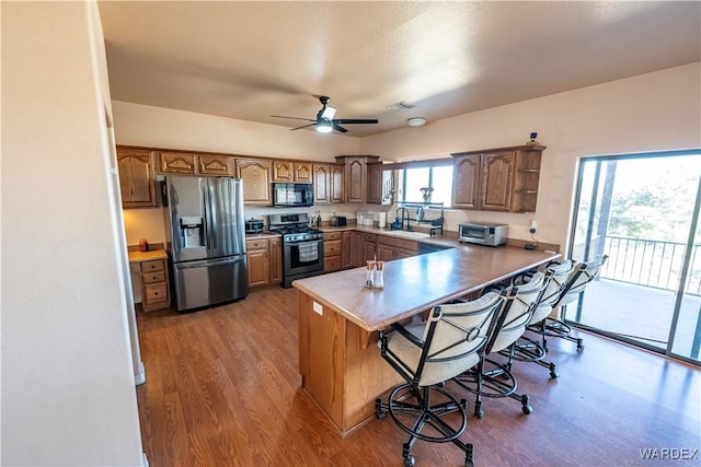 kitchen featuring visible vents, a breakfast bar, wood finished floors, a peninsula, and stainless steel appliances