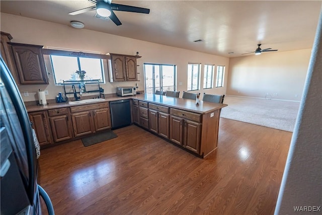 kitchen featuring dishwashing machine, dark wood-type flooring, freestanding refrigerator, a peninsula, and a sink