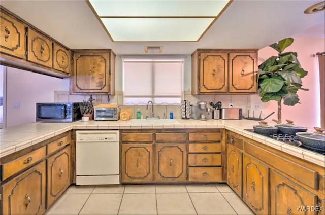 kitchen with a sink, tile counters, brown cabinets, dishwasher, and stainless steel microwave