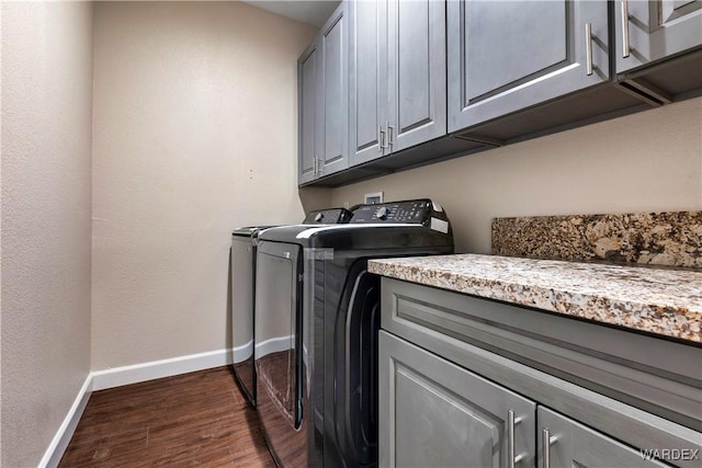 laundry room with cabinet space, baseboards, dark wood finished floors, and washing machine and clothes dryer