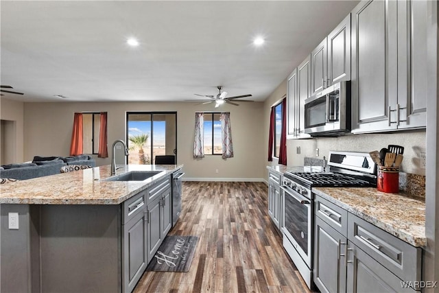 kitchen featuring a kitchen island with sink, stainless steel appliances, a sink, open floor plan, and gray cabinets